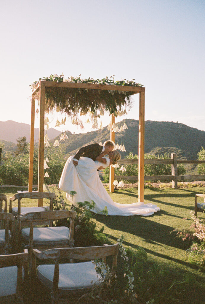 Newlyweds kissing at sunset with panoramic Malibu vineyard backdrop